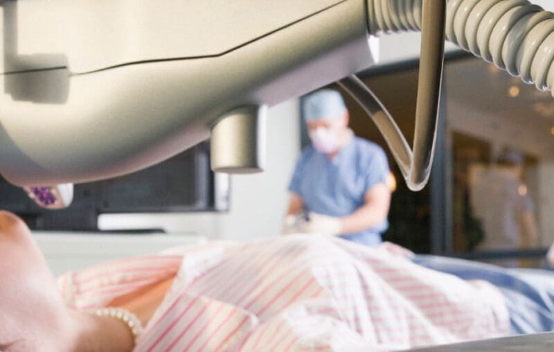 A surgeon is operating on an animal in the background.