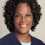A woman with curly hair and blue shirt smiling.
