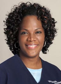 A woman with curly hair and blue shirt smiling.